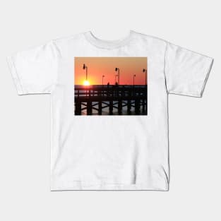 Two fishermen sillouhetted on the pier at sunrise Kids T-Shirt